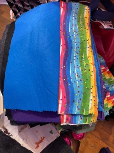 A stack of colorful fabric pieces including blue, rainbow striped, and patterned fabrics.